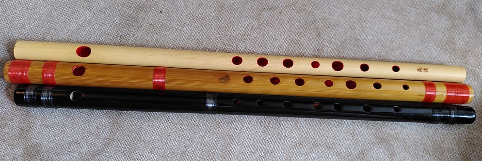 Three Japanese bamboo flutes.  One is simple, made of clear bamboo and lacquered red inside.  The next is smoked bamboo with what looks like red strings, but turns out to be tape. The third is all black.